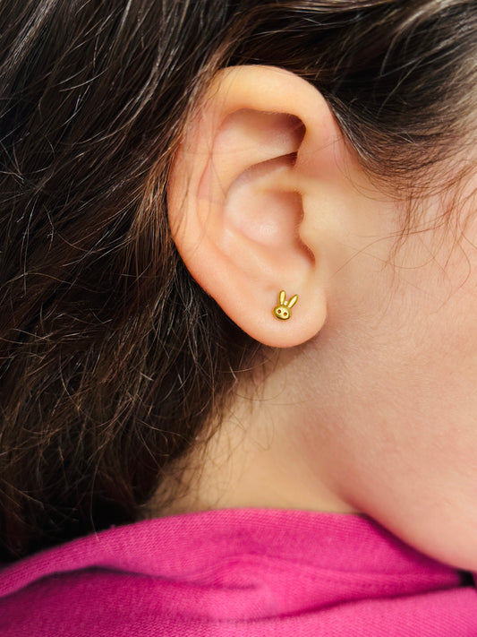 Gold Tiny Bunny Studs shown on a girl’s ear, close up to show detail and size