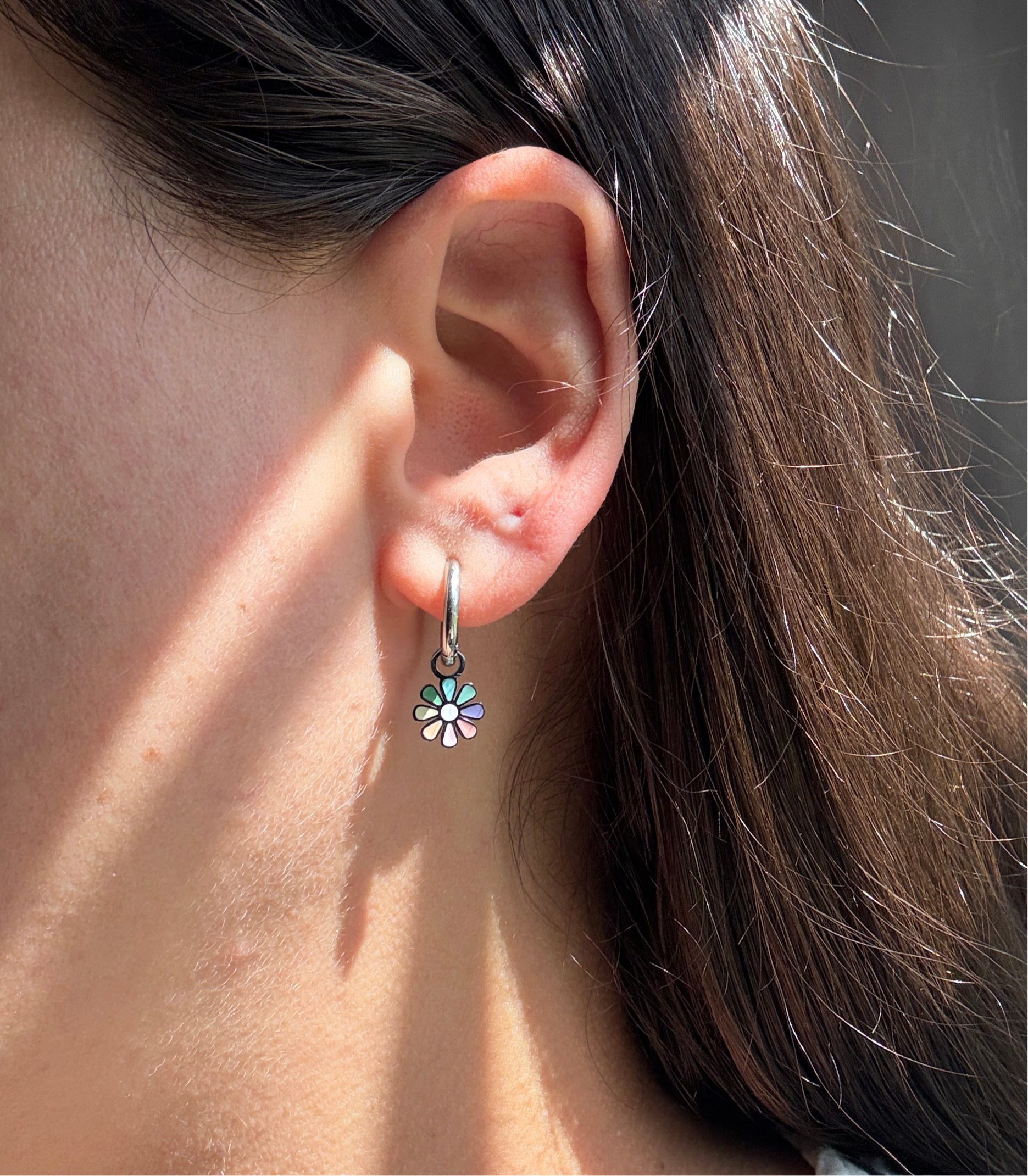 Close-up of an ear wearing a floral earring with sunlight casting shadows.