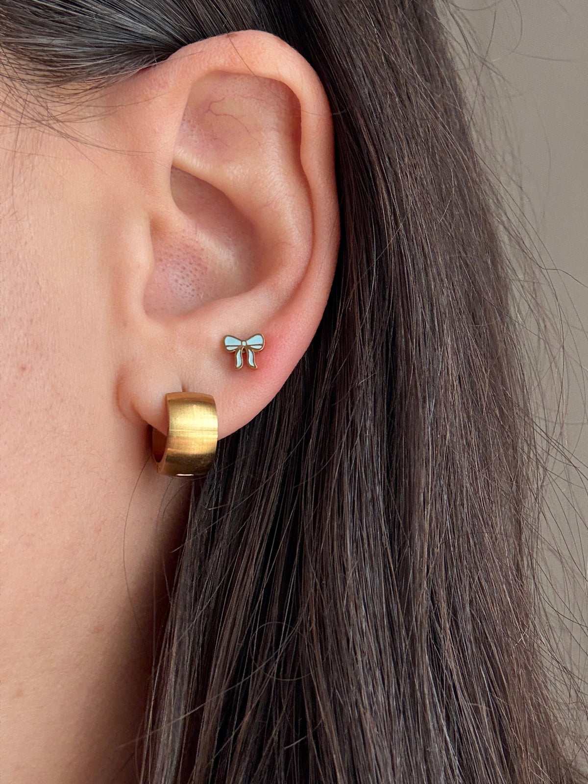 Baby blue and gold bow Screwback studs Stacked with chunky gold Huggie hoops worn on an ear