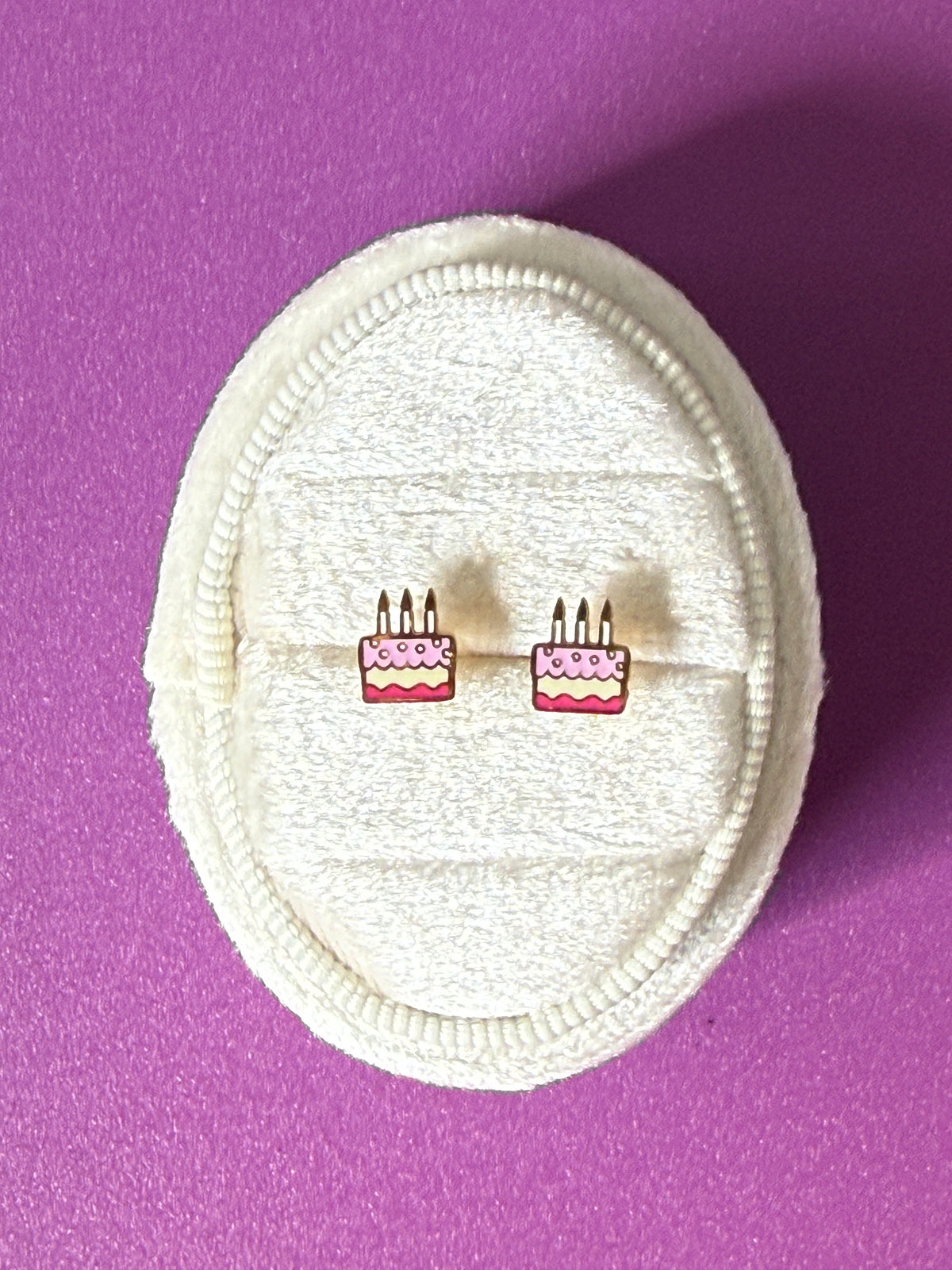 Birthday cake studs Shown over a white velvet oval jewelry box, showing enamel color details