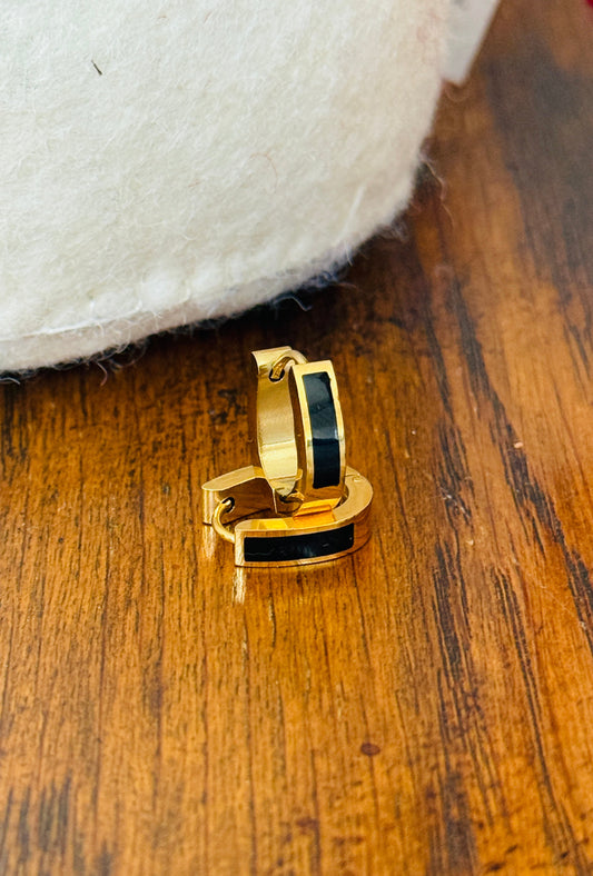 Gold hoop earring with black enamel strip  on a wooden surface