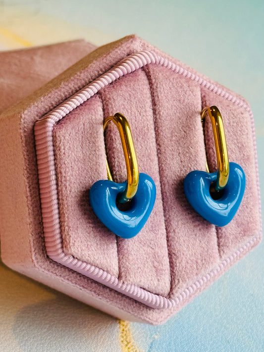 Blue heart-shaped earrings with gold hooks on a pink jewelry box.