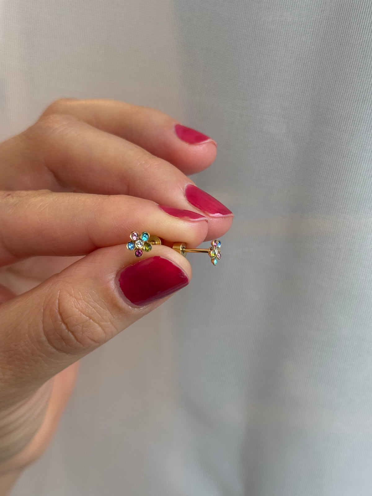 Colorful Flower Crystals Studs Being held between 2 adult fingers to show screwbacks and sparkle details