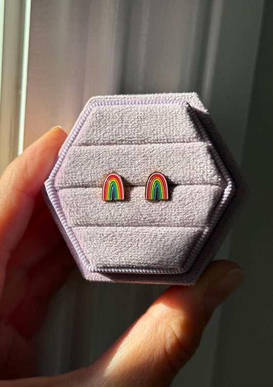 Rainbow screwback studs shown on a light purple velvet box under direct sunlight