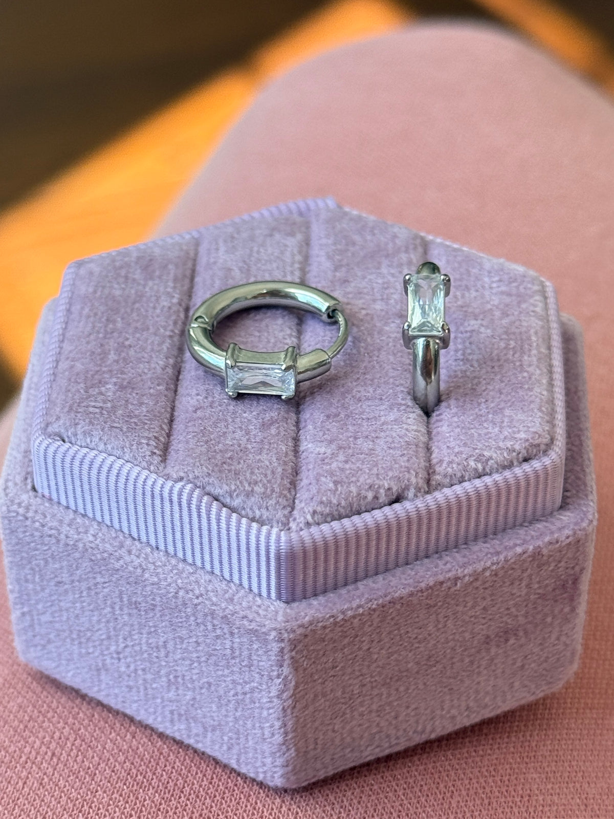 Two silver rings with a baguette zirconia in a purple jewelry box on a pink surface.