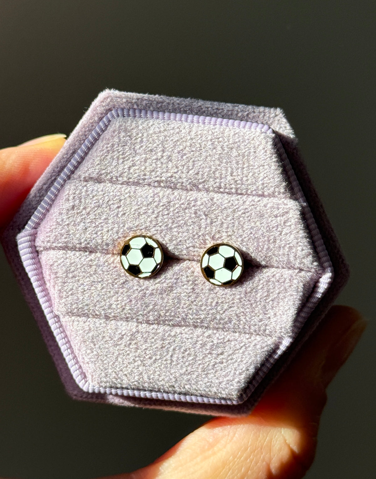Pair of soccer ball studs shown under direct sunlight on a light purple velvet box
