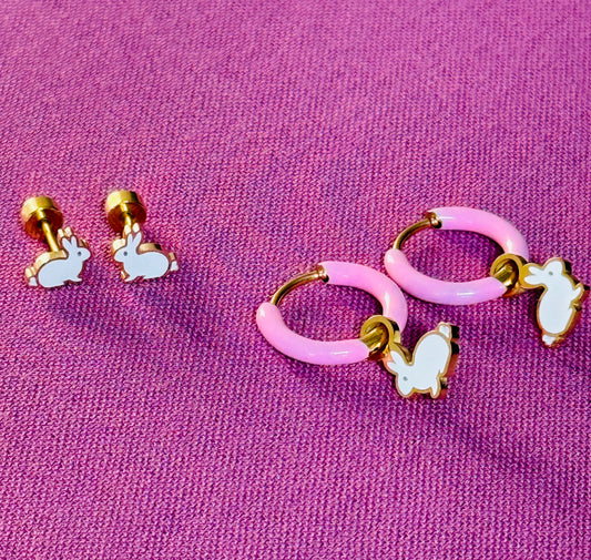 Set of pink hoop earrings with gold accents and white butterfly charms on a purple fabric background.