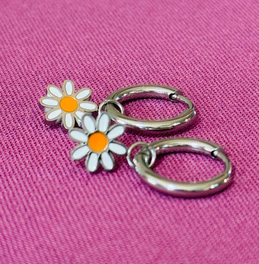 Silver hoop earrings with daisy flower charms on a pink fabric background