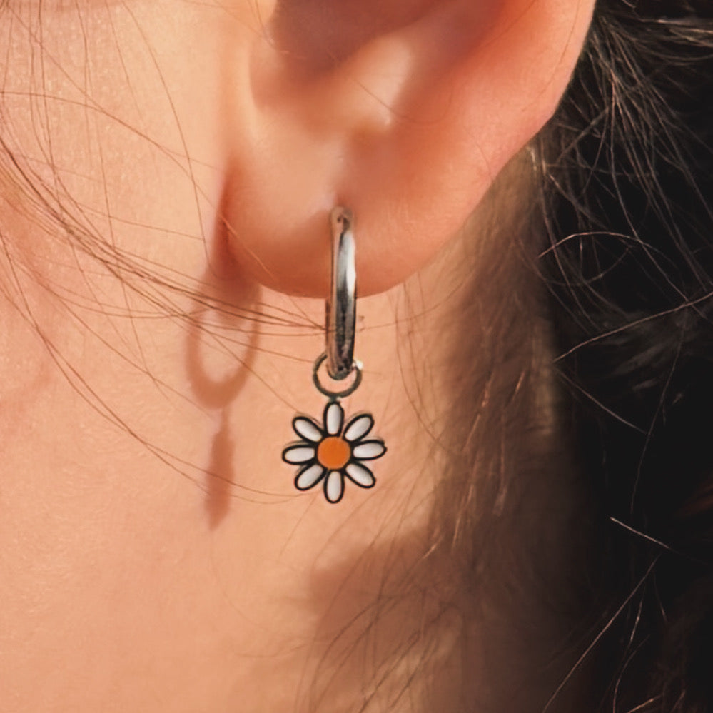 Close-up of an ear wearing a silver hoop earring with a daisy charm.