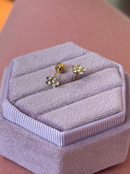 Gold flower-shaped earrings on a lavender jewelry box
